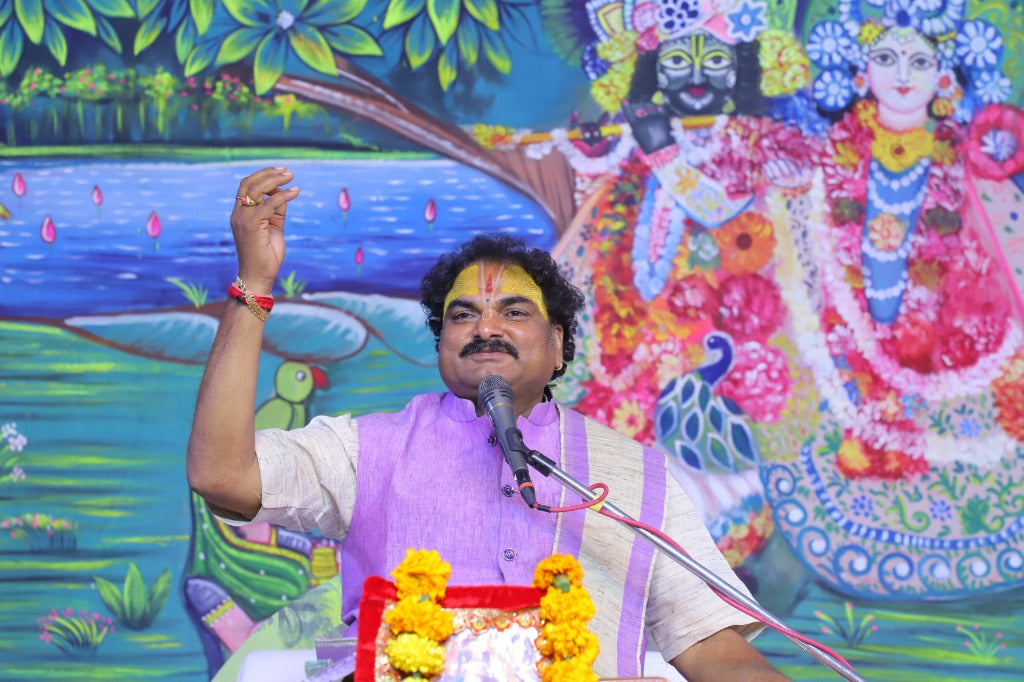 Acharya Shrikant Tripathi Ji conducting Shrimad Bhagwat Katha with Radha Krishna backdrop